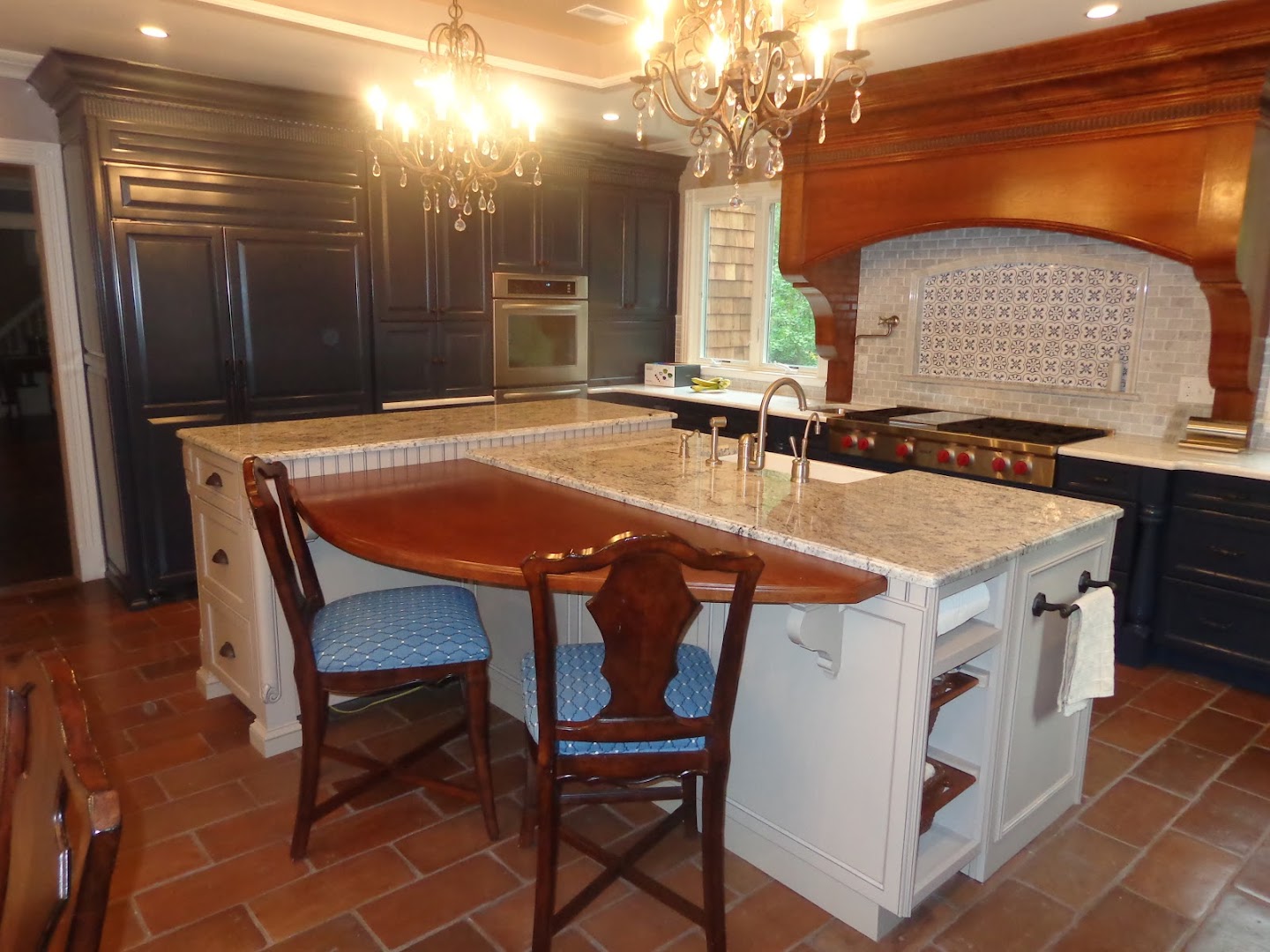 A custom-built traditional kitchen with crystal chandeliers, dark wood cabinetry, and a granite island